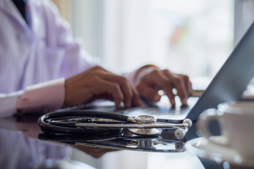 Clinical employee working on laptop with stethoscope on desk